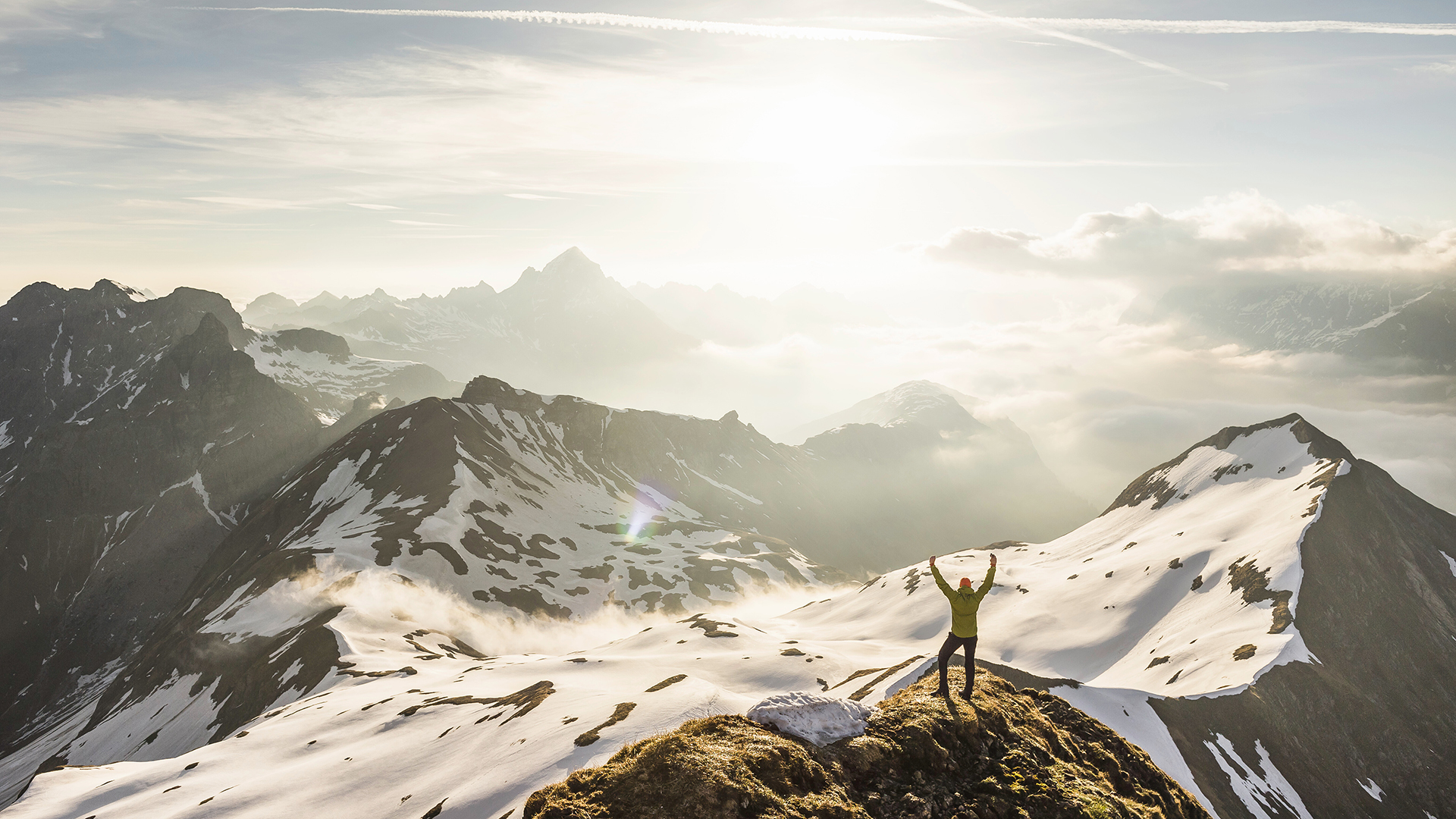 Adventurer celebrating atop a snowy mountain peak at sunrise